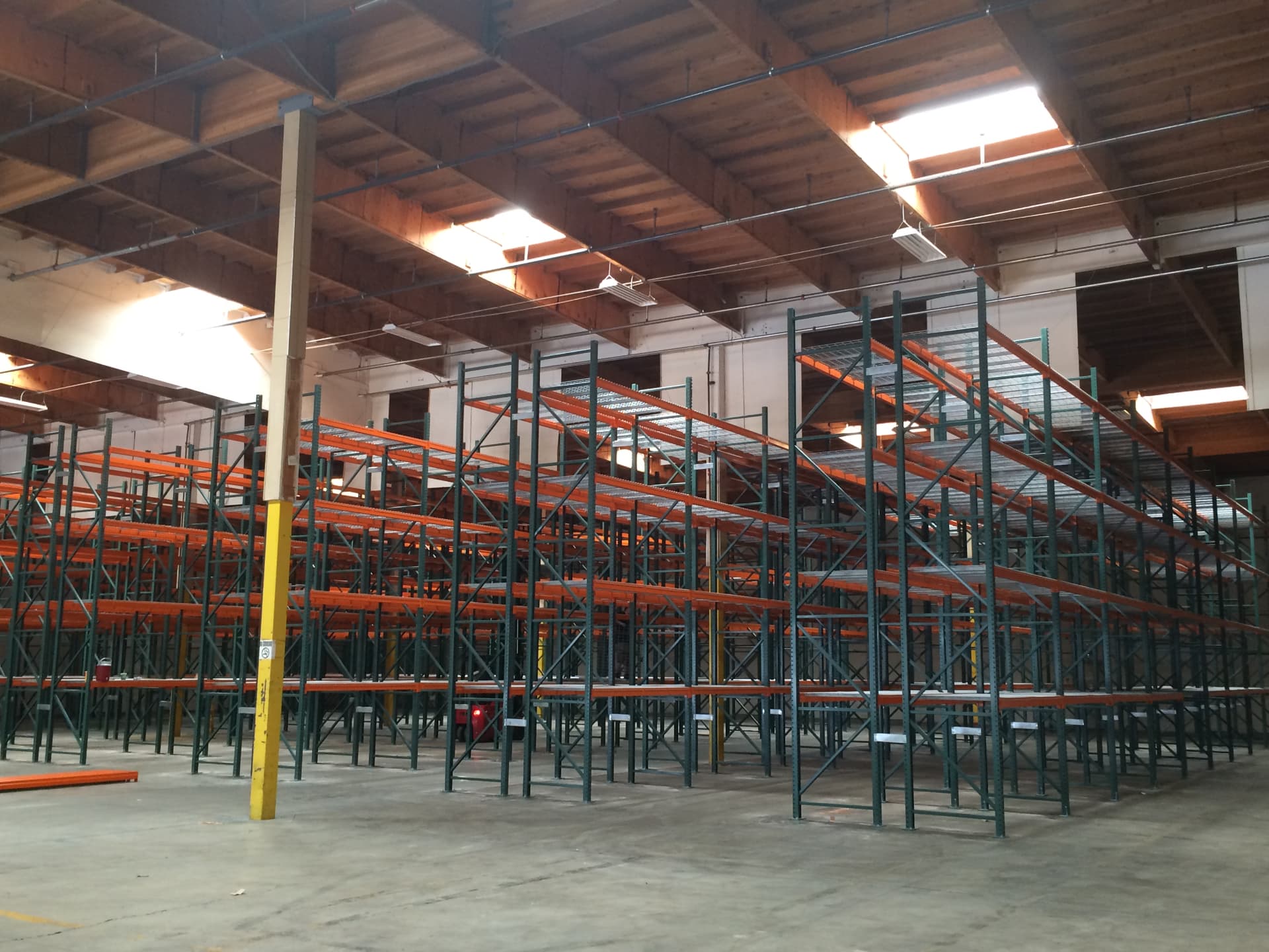 Rows of orange and green pallet racks inside a wooden-ceiling warehouse