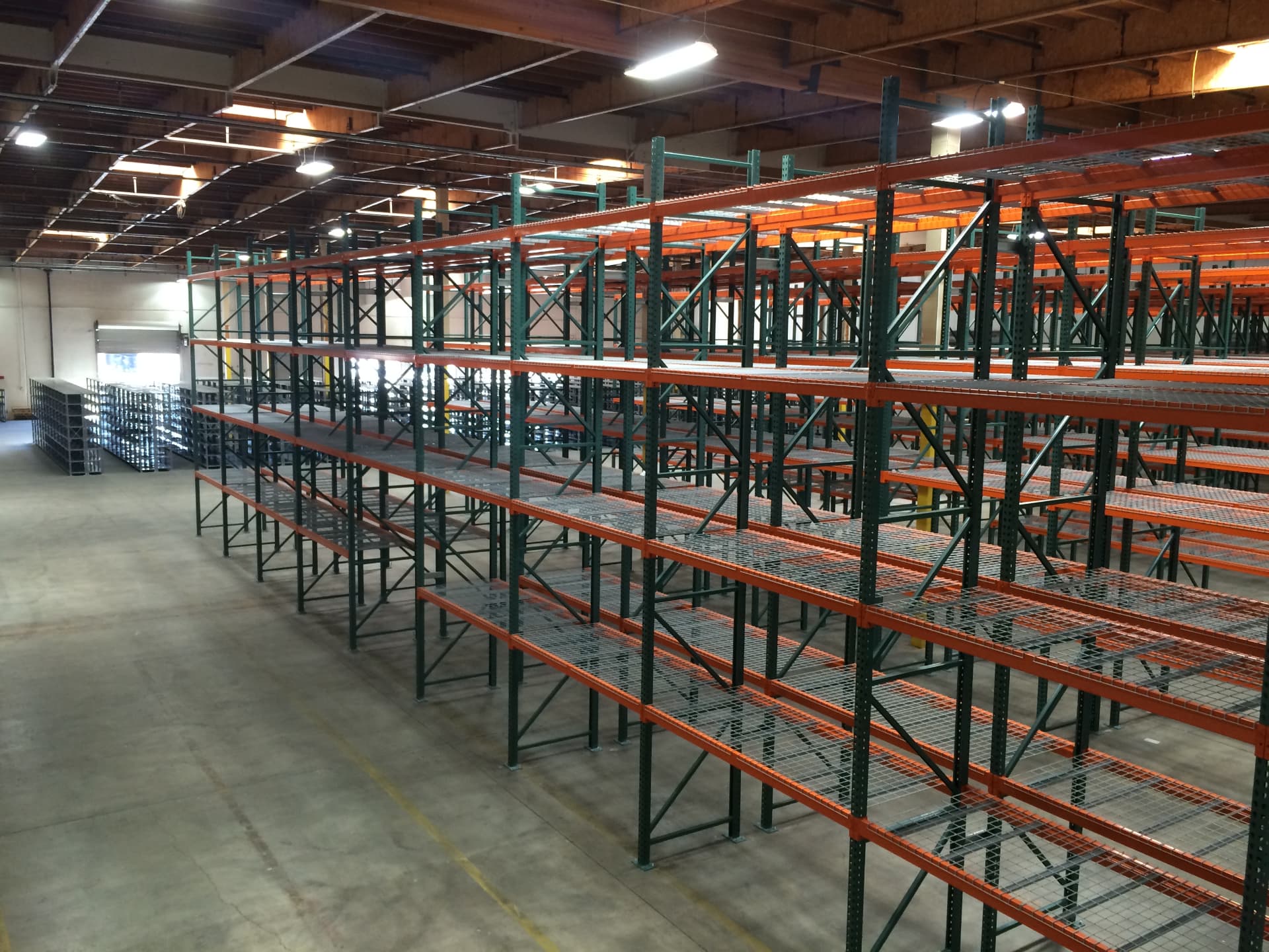 Long aisles of orange and green pallet racking with wire decking